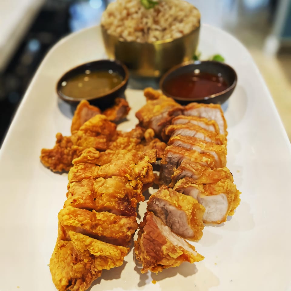 Crispy fried pork belly slices with two dipping sauces and a bowl of rice on a white platter.