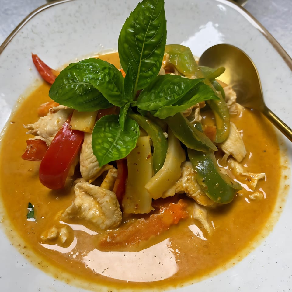 Thai red curry with chicken, red and green bell peppers, and basil on a white plate.