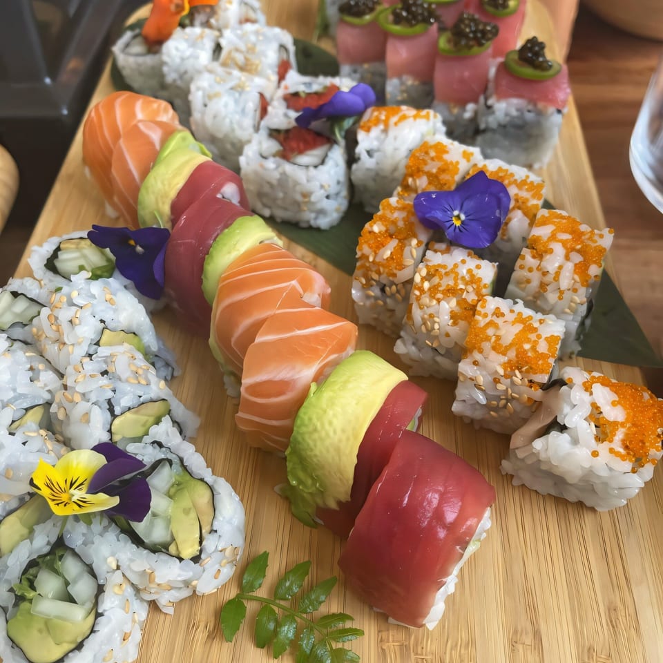 Assorted sushi rolls with salmon, tuna, avocado, and roe, garnished with edible flowers on a wooden board.